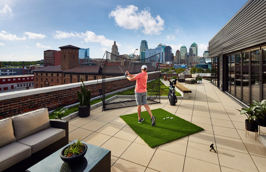 Golfer hitting into a practice net on a rooftop patio with a portable launch monitor tracking the shot from behind the mat