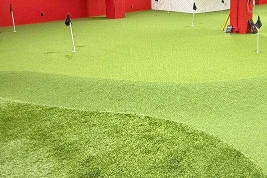 Contoured indoor putting green turf with a darker fringe and two practice flags inside a golf simulator facility